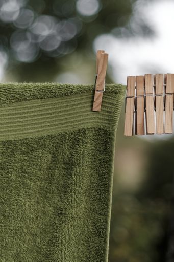 A vertical closeup shot of a green towel hanging on a washing line with wooden pegs on it