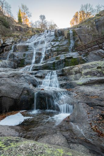 A vertical shot of a waterfall flowing in the forest in autumn