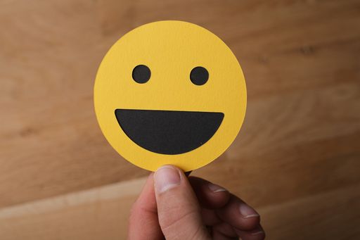A closeup shot of a man holding a laughing smiley face sign on a wooden background