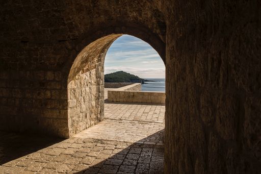 A beautiful shot of brick made arched doorway with a view of a sea and a forested mountain in the distance in Dubrovnik