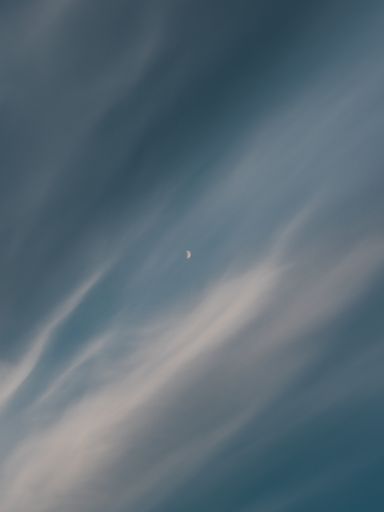 A vertical shot of a waxing crescent moon behind the clouds