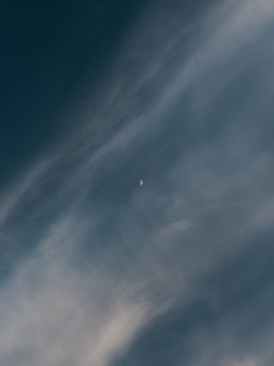 A vertical shot of a waxing crescent moon behind the clouds