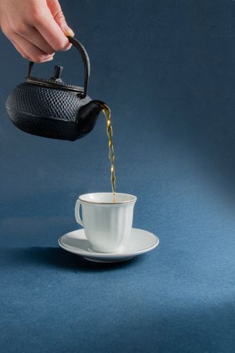 A portrait of a tea being poured from a teapot to a teacup on a black background