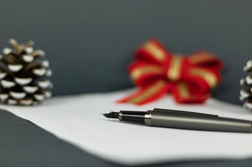 A macro of a pen lying on a white piece of paper with a blurry background of red bow and acorn