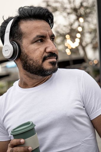 A vertical portrait of a bearded Hispanic man with headphones and coffee mug outdoors in Argentina