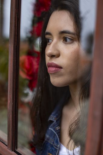 A vertical shot of a beautiful female looking outside from behind a window