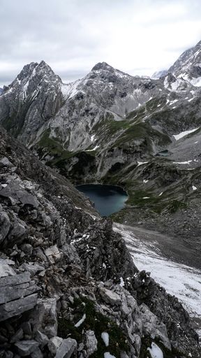 A vertical shot of a lake surrounded by mountains under a cloudy sky