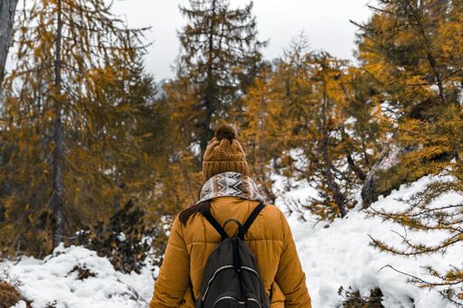 A Caucasian female hiker wearing winter clothes and a backpack walking on a snowy path in the forest