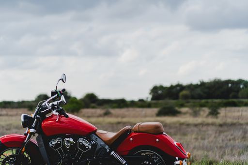 A closeup shot of a red motorcycle with a field in the blurry background