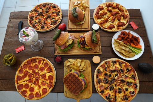 A high angle closeup shot of pizzas and burgers on a wooden table