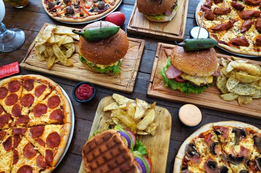 A high angle closeup shot of pizzas and burgers on a wooden table