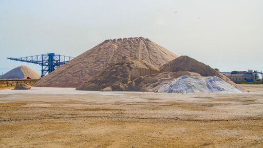 A blue crane in a quarry used for crushing sand for construction with a sandhill next to it