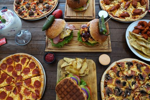 A high angle closeup shot of pizzas and burgers on a wooden table