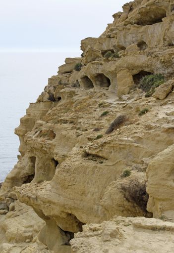 A vertical low angle shot of the beautiful rocky cliffs by the water captured in Crete, Greece