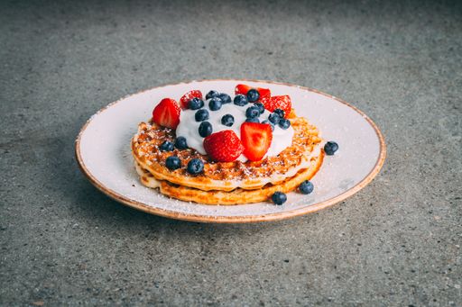 A Closeup of pancakes with cream and berries served on a white plate