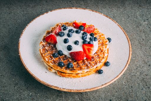 A closeup of pancakes with cream and berries served on a white plate