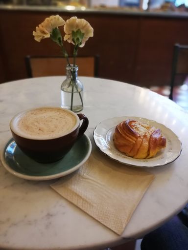 A vertical of a hot chocolate and a saffran bulle on a table with a glass vase of flowers