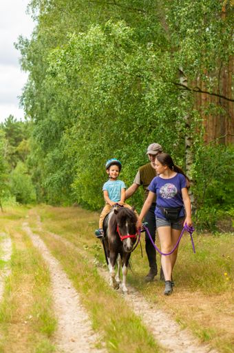 A young boy riding a small pony while instructor is leading on a footpath at a forest in the city of Baranowko, Poland