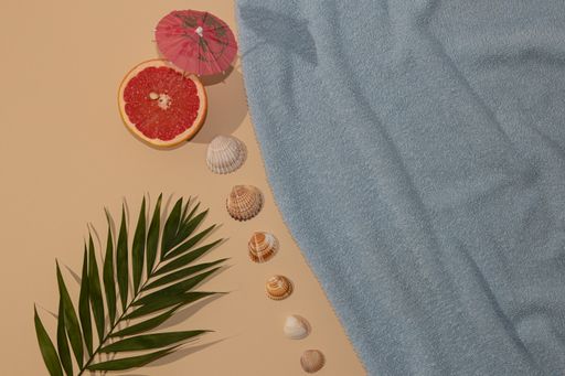 A top view of summer scene with a blue beach towel and palm leave and grape with parasol with seashells - Refreshment concept flat lay
