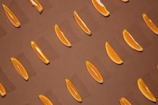 A top view of colorful fruit pattern of fresh orange slices with leaves on a brown background - Minimal flat lay