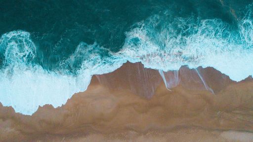 An aerial shot of sea waves hitting the sandy shore