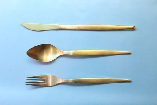 A high angle shot of a gold fork, spoon, and knife on a blue surface