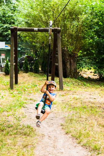 A vertical shot of a young boy holding on a zipper line at a playground