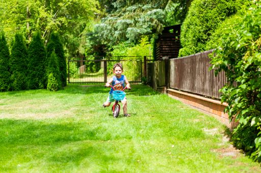 A view of a young boy practicing to ride a bike on green grass field