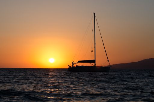 The silhouette of a fishing boat off the coast of Mykonos, Greece against a bright setting sun