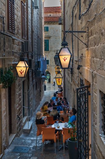 A vertical shot of an open-air restaurant with people sitting at the table in Old Town Street, Dubrovnik, Croatia