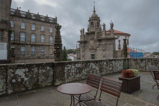 A perspective shot of wooden chairs and table in the background of a cathedral in Santiago de Compostela.