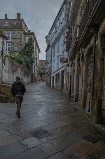 A vertical shot of a person walking near the buildings in Santiago de Compostela, Spain.