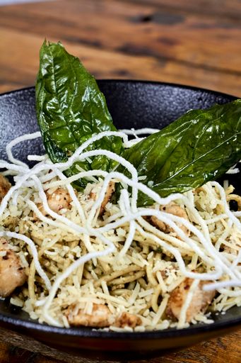 A selective focus shot of pasta with chicken made of rice noodles on a black plate
