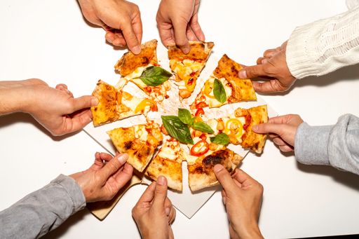 A top view of hands taking slices from the whole pizza