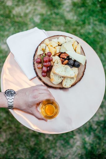 A vertical selective overhead shot of a person holding a glass near bread and fruits on a white plate