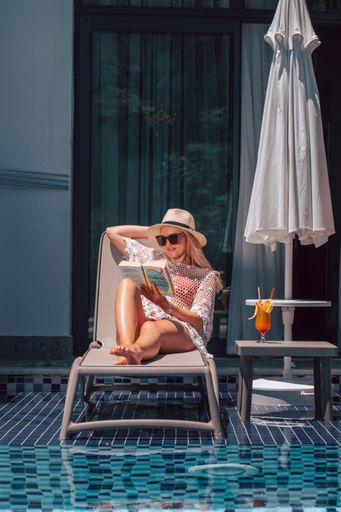 A vertical shot of a white Caucasian girl posing for a picture while reading a book near the pool