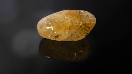 A closeup of a natural gemstone - pebble of citrine mineral gemstone on a reflective surface