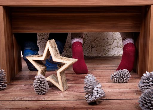 Feet of couple sitting at home on a brown bench wearing wool socks with christmas decoration in front like a star out of wood and pine cones