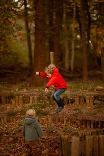 A vertical of two Caucasian children jumping and playing together in a foliage forest