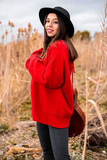 A beautiful Caucasian female wearing a black hat and holding a guitar in the field