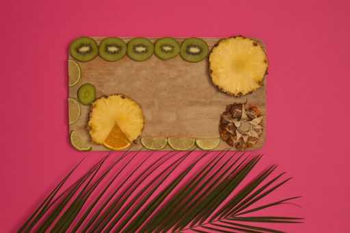 A top view of two glasses and tropical fruits on wood with pink background