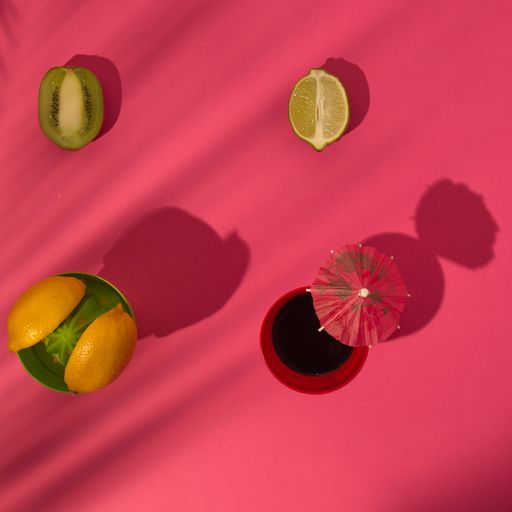 A top view of lemon, kiwi, oranges, and a glass with parasol on a pink background