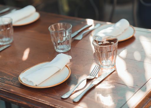 A selective focus shot of a wooden table with plates, glasses, and forks