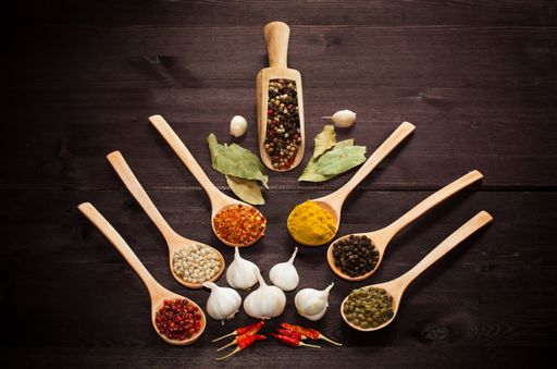 A top view of fresh garlic bulbs with different spices in wooden spoons on the table