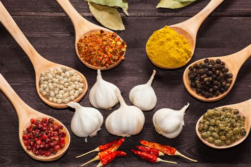 A top view of Various exotic spices in spoons and white garlic on a wooden table