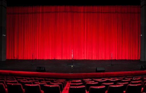 An empty stage with closed red curtains and a wooden floor