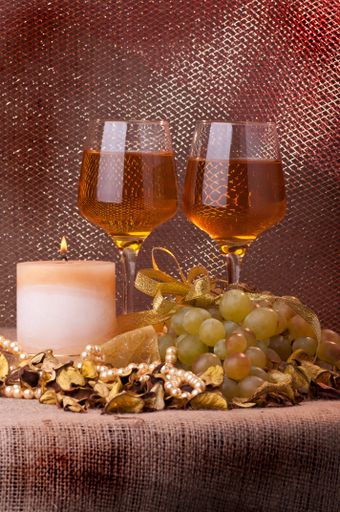 A vertical shot of two glasses of wine with ripe grapes and a burning candle on the table