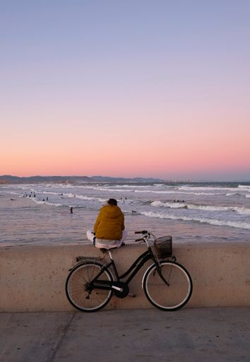 A man with a bicycle sitting on the stone and looking at the waves of sea in Valencia, Spain