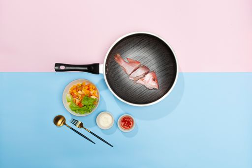 A flat lay of a frying pan with a fresh fish cut into pieces and a bowl of salad on the table