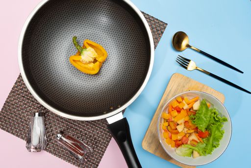 A flat lay of a frying pan with cooking ingredients and a bowl of tasty salad on the table